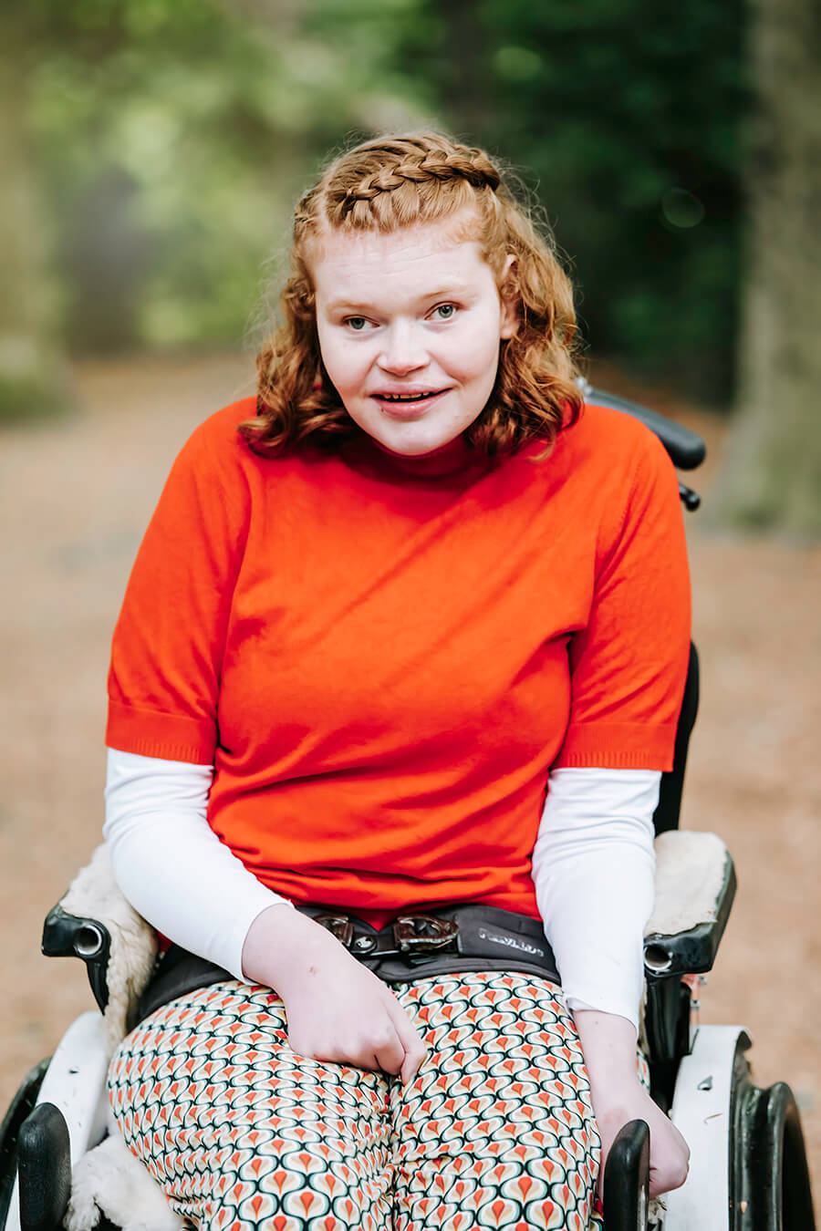 Elfie van voren op de foto in haar rolstoel. Ze kijkt vriendelijk in de lens.