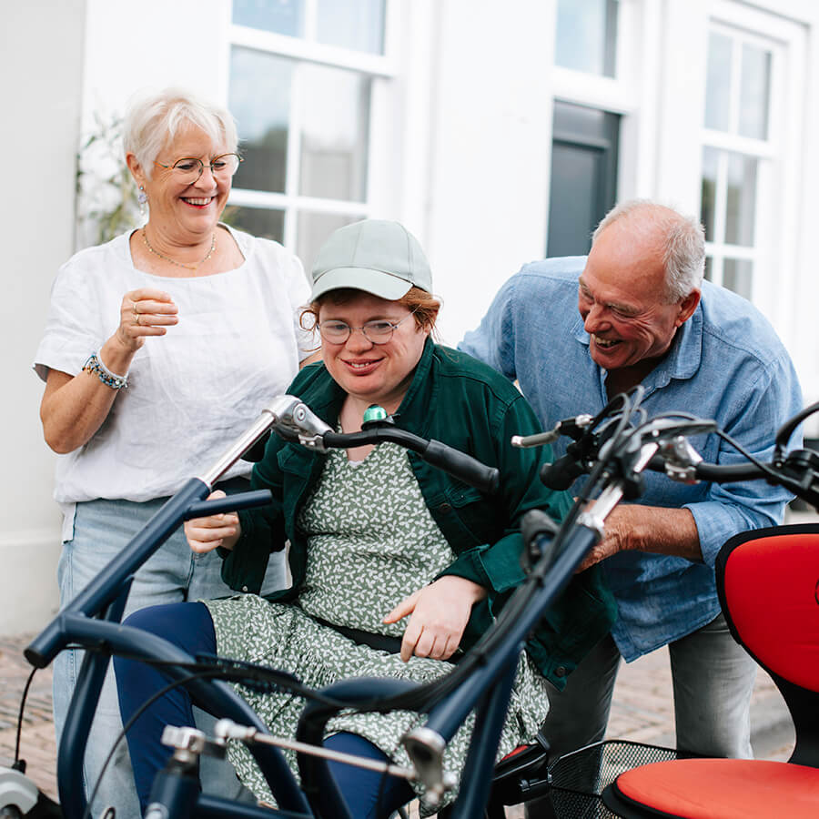 Loes met haar ouders bij de duofiets. Ze lachen samen terwijl Loes op het zadel zit.