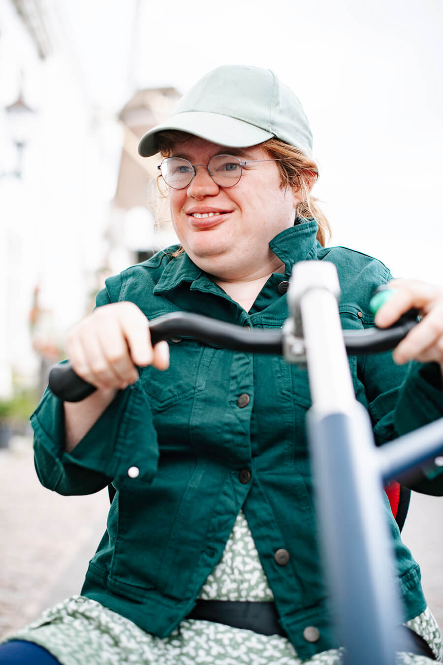 Een close-up van Loes op de fiets. Ze lacht met een pet op.