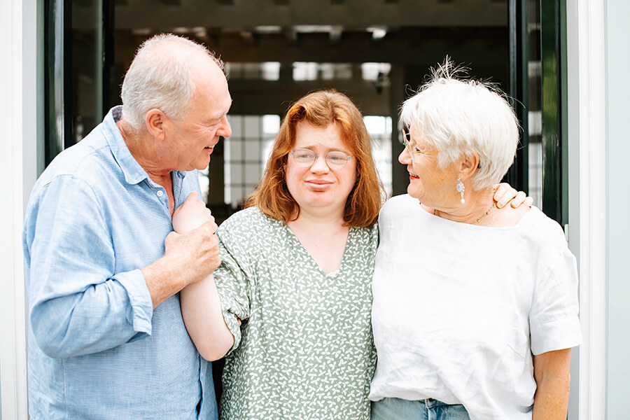 Loes met haar ouders in de deuropening. Vader houdt haar pols vast.