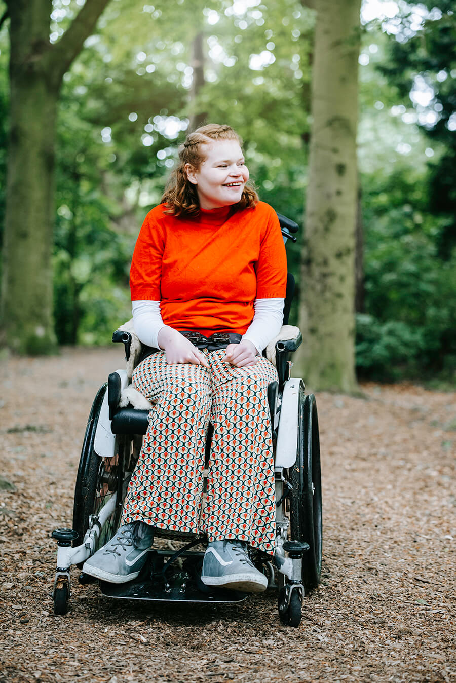 Elfie is naar rolstoel in het bos. Zij kijkt lachend om zich heen.