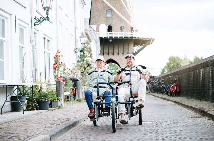 Loes op de duofiets, samen met haar begeleider, rijdend door het historische centrum van Wijk bij Duurstede.