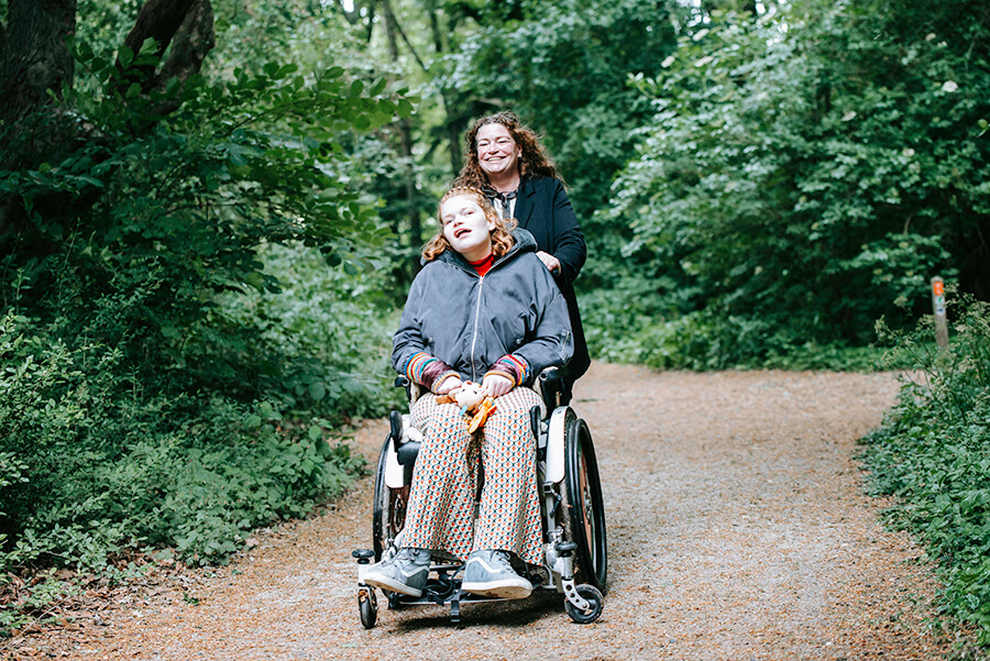 Elfie en haar moeder samen in het bos. Elfie wordt voortgeduwd in haar rolstoel.