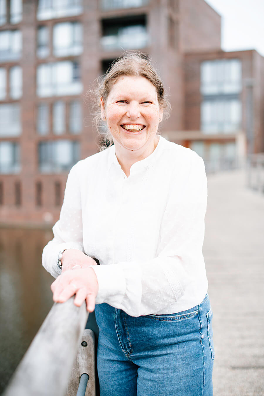 Joline leunt lachend tegen de railing van een brug en kijkt recht in de camera.