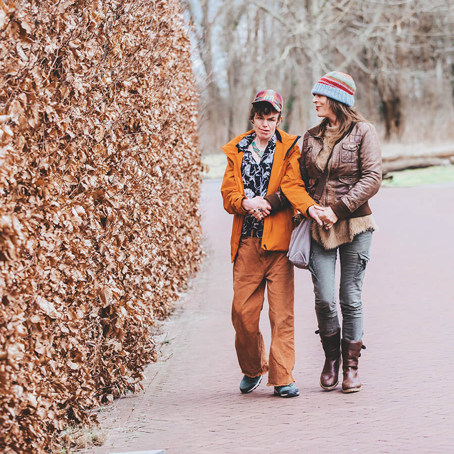 Thiandi en haar moeder lopen op straat langs een heg. Het is herfst en ze hebben mutsen op.